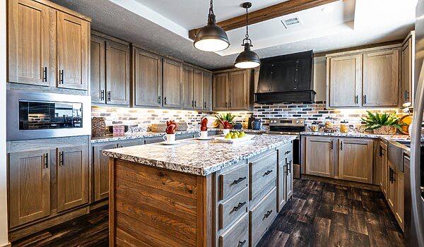 Spacious kitchen with wooden cabinets, marble island, and dark wood floors. Two pendant lights hang above, creating a warm, inviting atmosphere.
