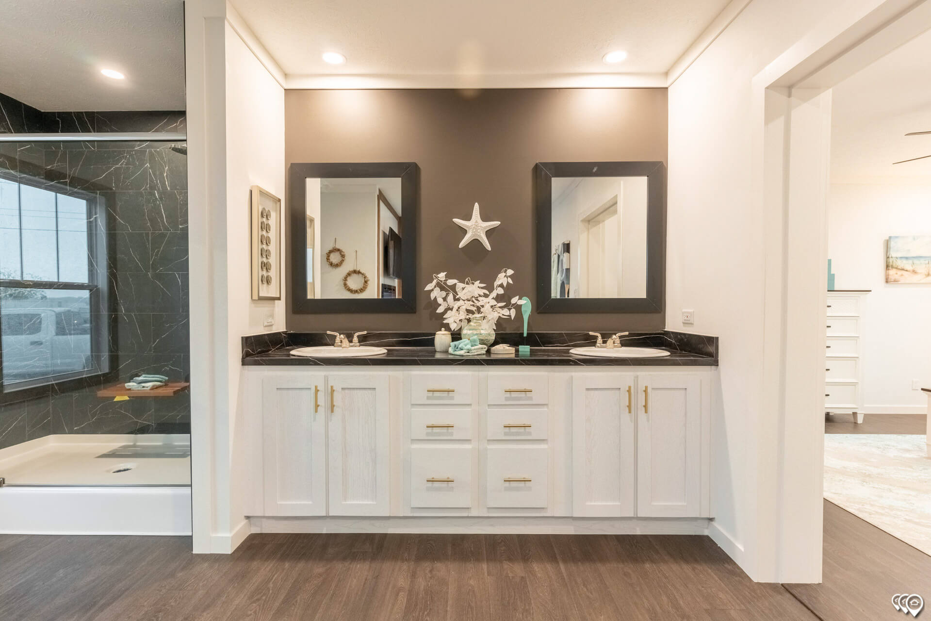 Modern bathroom with dual white sinks and black countertops. Two mirrors hang above, and a starfish decorates the wall. Elegant and clean design.