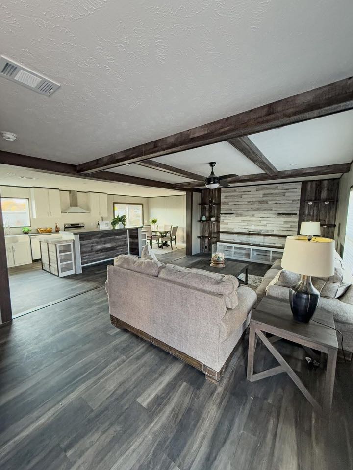 Modern living room with hardwood floors, gray sofas, and a wooden coffee table. Adjacent open kitchen features white cabinets and an island. Cozy and inviting atmosphere.
