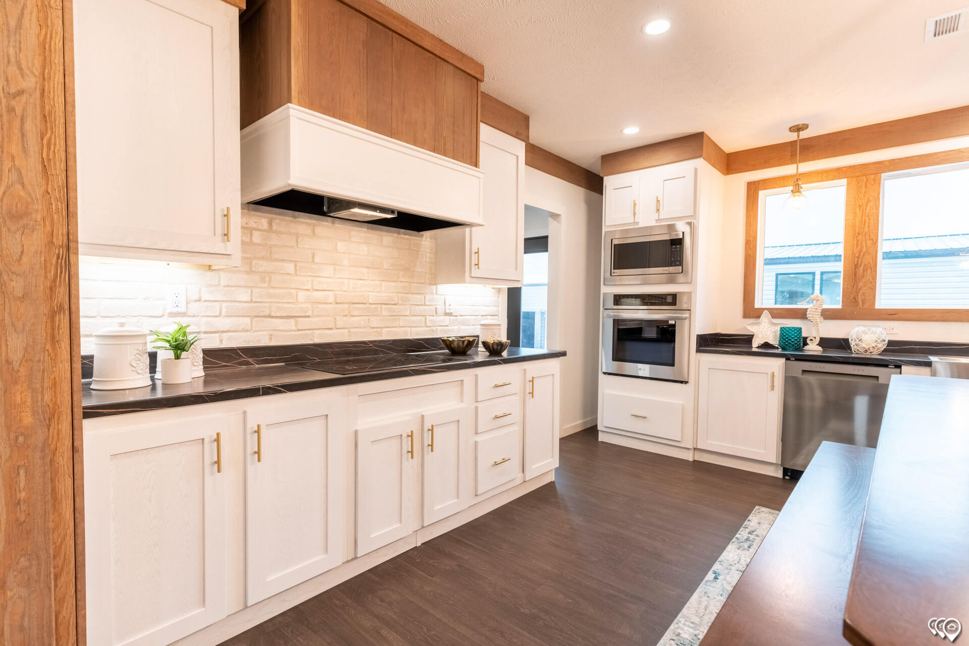 Modern kitchen with white and wood cabinets, dark countertops, and a tile backsplash. Stainless steel appliances and pendant light add a sleek touch.