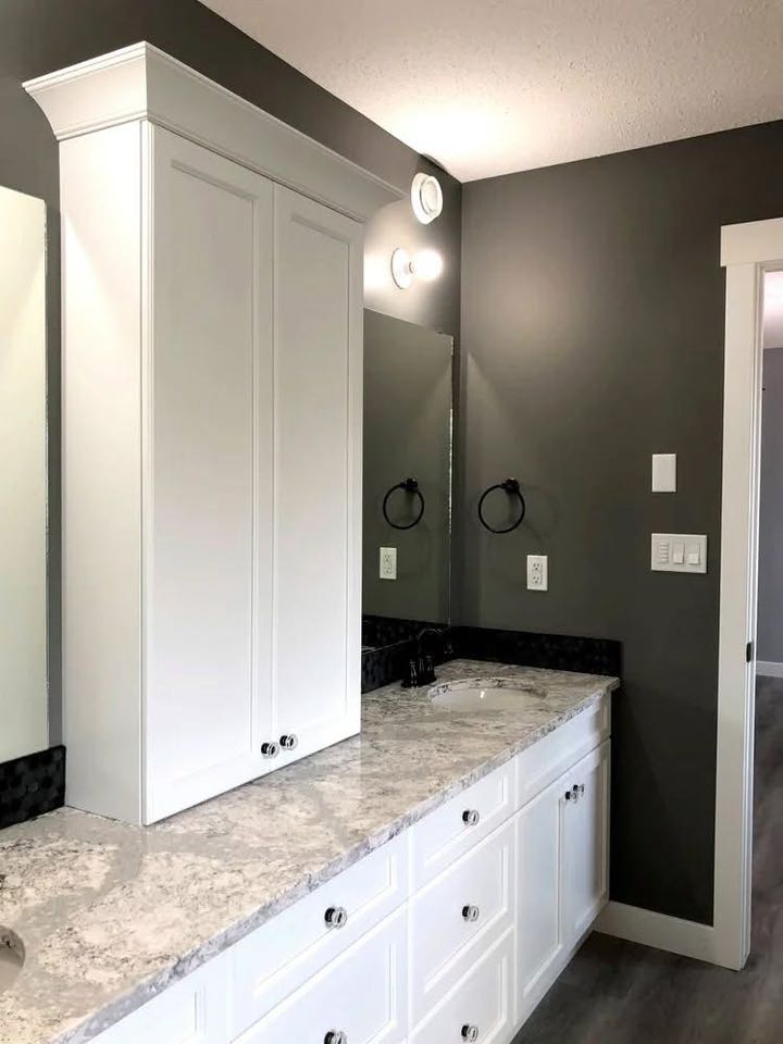 Modern bathroom with white cabinets and a marble countertop. A large mirror above the sink reflects warm lighting. Gray walls add a sleek touch.