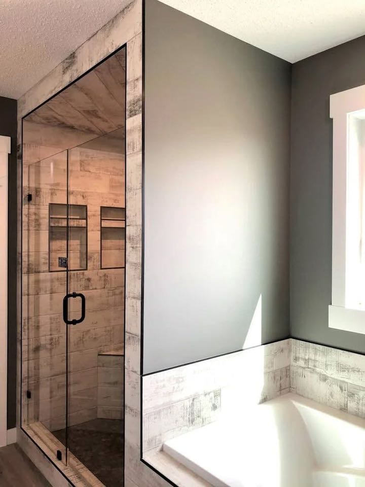 Modern bathroom with a sleek, glass shower enclosure. Light wood accents and gray walls create a calm, minimalist atmosphere. Bright natural lighting.