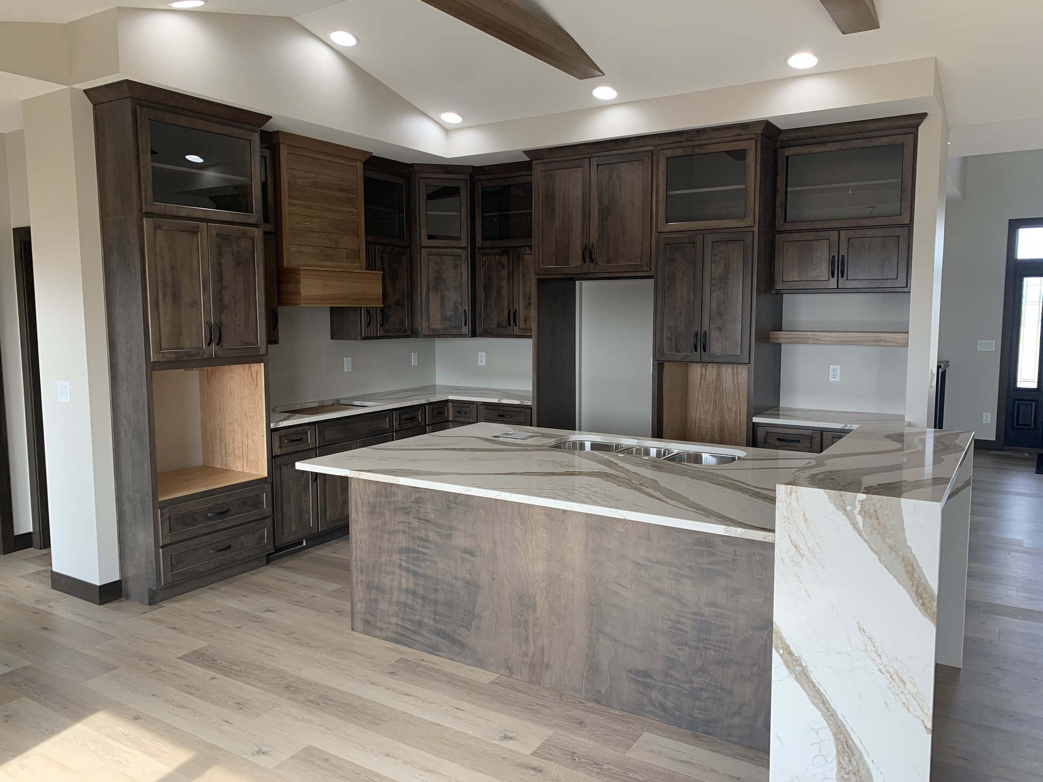 Modern kitchen with dark wood cabinets and a large marble island. Recessed lighting creates a bright, welcoming space. Neutral tones convey elegance.