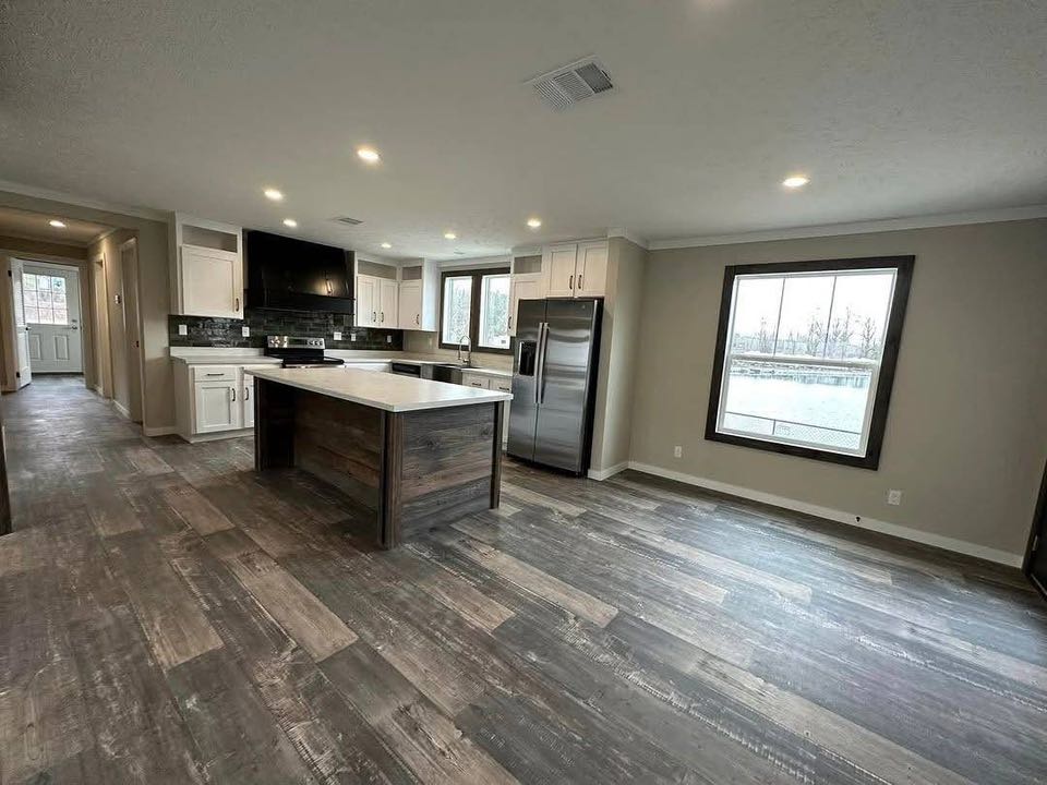 Spacious modern kitchen with wood-patterned floors, a large island, stainless steel appliances, white cabinets, and gray walls, creating a cozy ambiance.