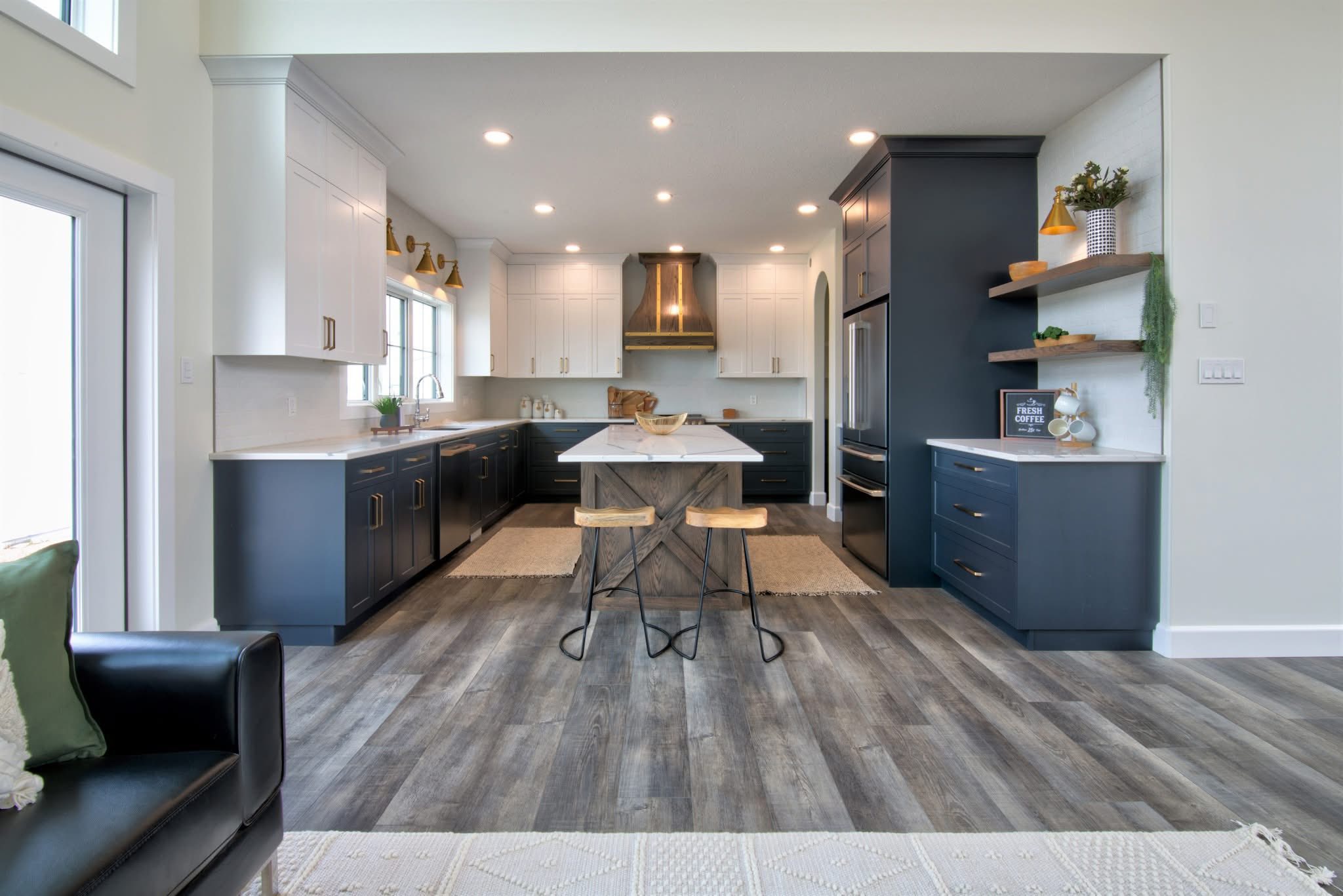Modern kitchen with a sleek design. Features two-toned cabinets, white and dark gray, with gold accents, a center island, and wood flooring. Bright and inviting ambiance.