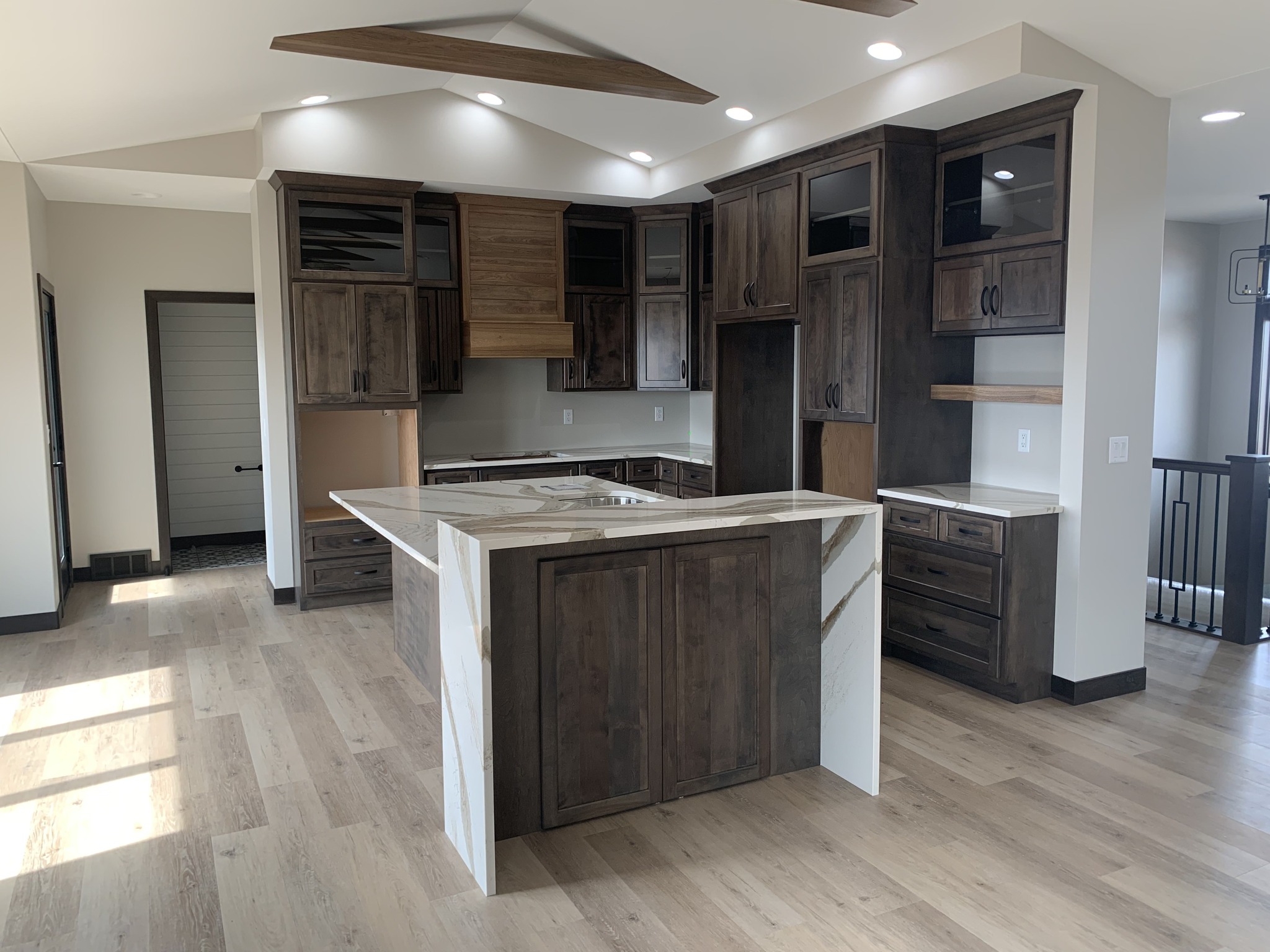 A modern kitchen with dark wood cabinets and a central island featuring a marble countertop. Bright, open design with light wood floors and recessed lighting.