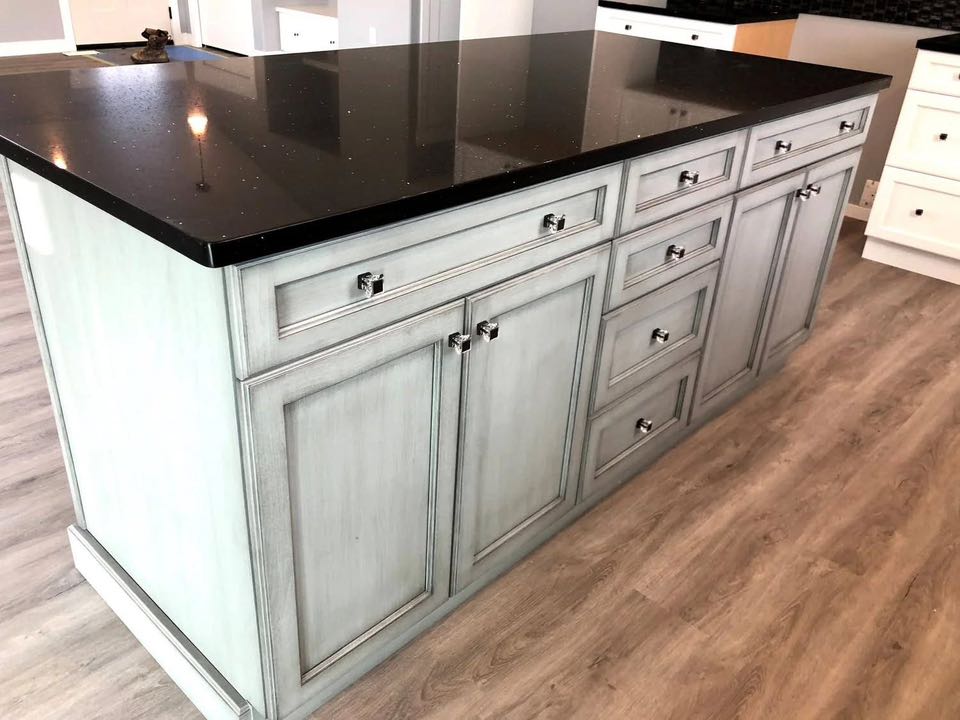 A kitchen island with light blue cabinets and drawers, featuring chrome handles, topped by a polished black countertop. The ambiance is modern and sleek.