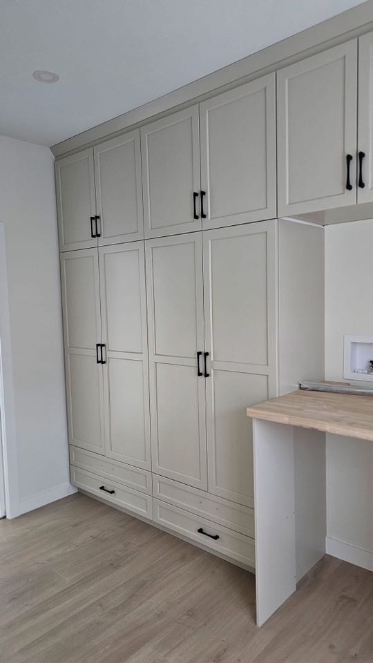 Tall, beige cabinets with black handles span the wall, paired with a light wood countertop. The setup conveys a modern and organized kitchen vibe.