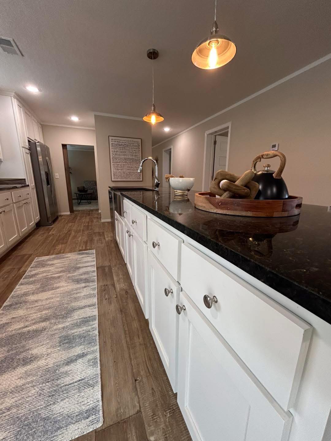 Modern kitchen with white cabinets, black countertops, and warm wooden floors. Two pendant lights hang above, creating a cozy, inviting atmosphere.