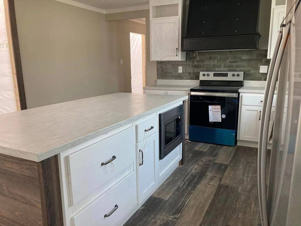 A modern kitchen with white cabinets, stainless steel appliances, and a black range hood. Features include a beige countertop and wood-style flooring. Cozy and clean atmosphere.