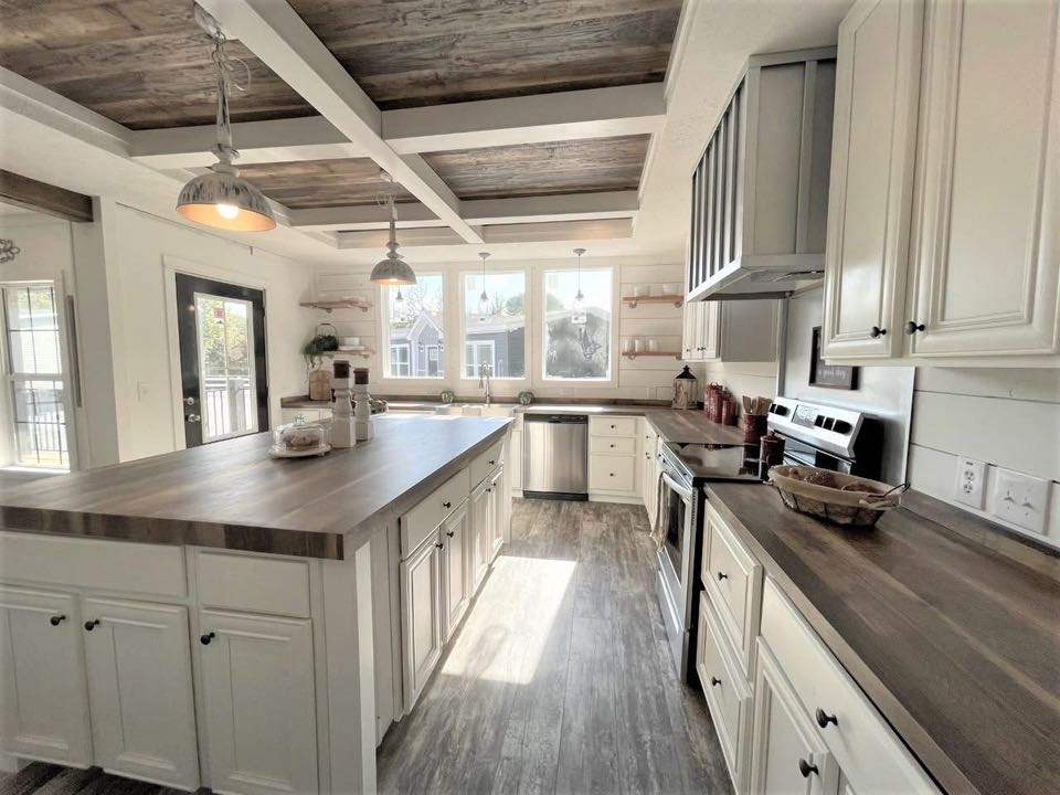 Spacious kitchen with rustic charm, featuring wooden countertops, white cabinets, pendant lighting, and large windows bringing in natural light. Cozy and inviting atmosphere.