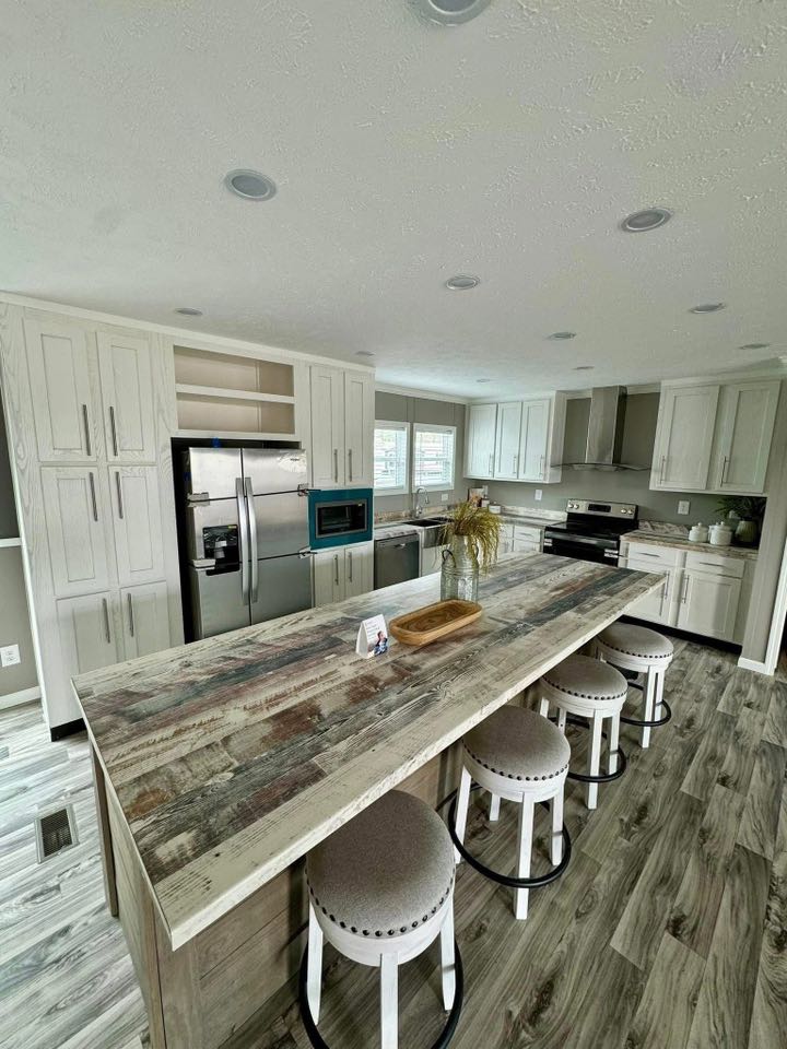 Spacious kitchen with rustic wood island and four stools. Light cabinets, stainless steel appliances, and large windows create a bright, inviting atmosphere.