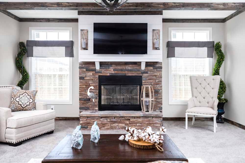 Elegant living room with a stone fireplace, wall-mounted TV, and neutral tones. Features plush armchairs, decorative plants, and soft lighting.