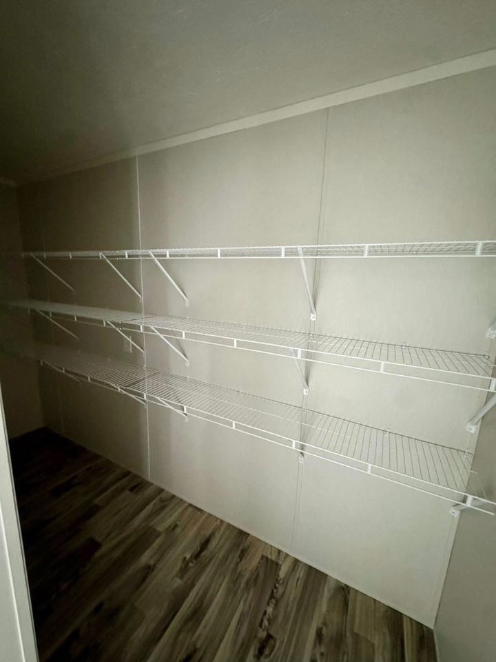 Empty white wire shelves mounted on a beige wall in a small room with wood-patterned flooring, creating a minimalist and organized space.