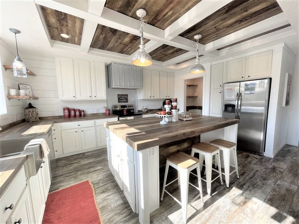 Modern farmhouse kitchen with white cabinets, wood countertops and ceiling beams, and stainless steel appliances. Island with stools and pendant lights. Cozy and bright.