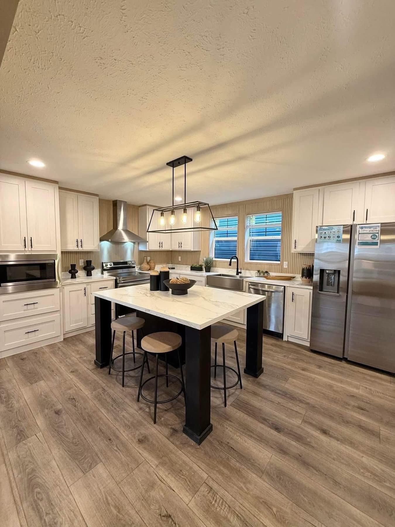 Modern kitchen with white cabinets, stainless steel appliances, a central island with black stools, and a geometric light fixture. Warm, inviting atmosphere.