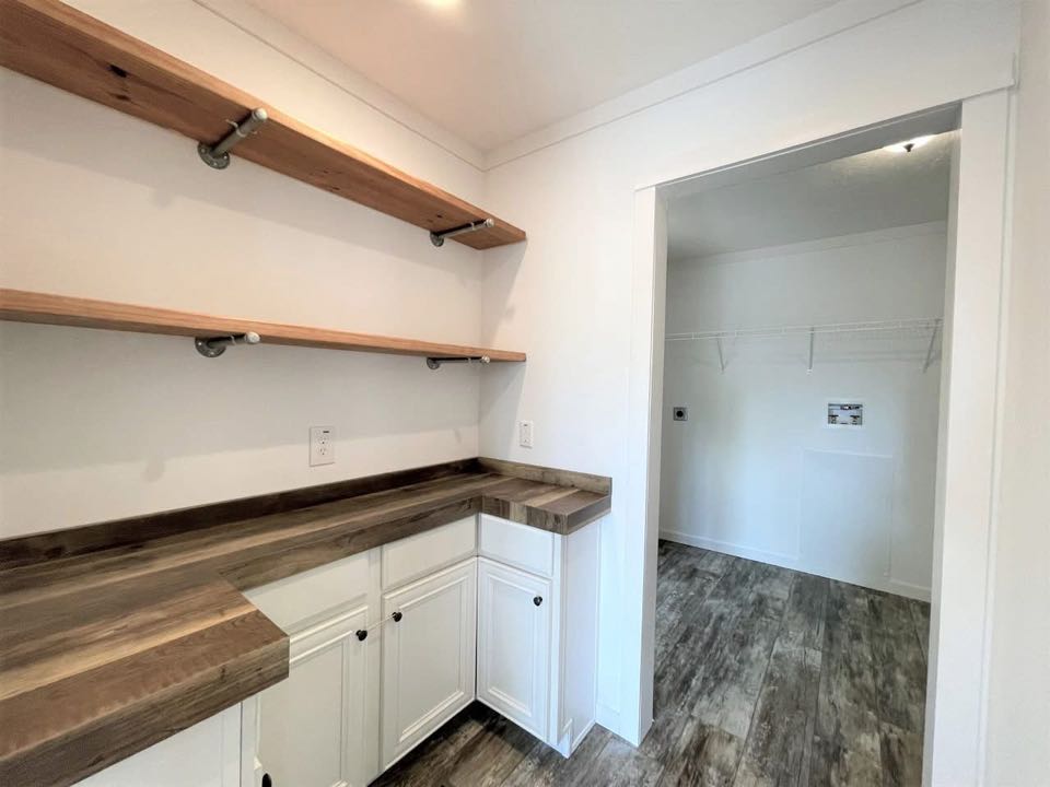 A bright utility room features wooden countertops, white cabinets, open wooden shelves, and adjacent laundry space with wooden flooring, creating a clean, modern feel.