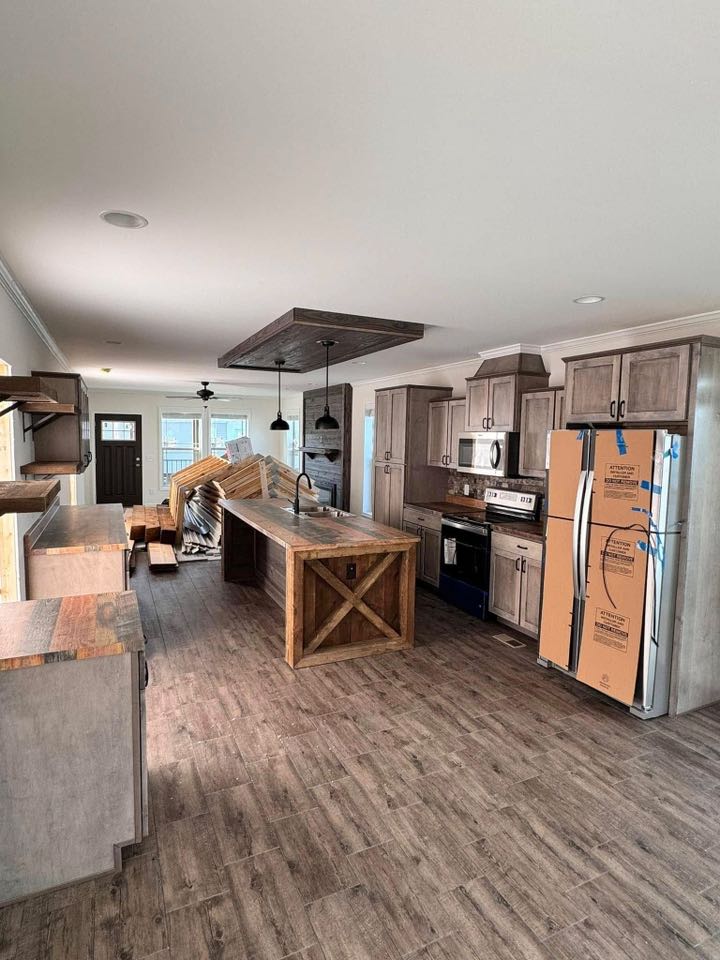 Newly renovated kitchen with rustic wooden cabinets and island under pendant lights. Kitchen appliances and panels are unpacked, creating a modern yet unfinished look.