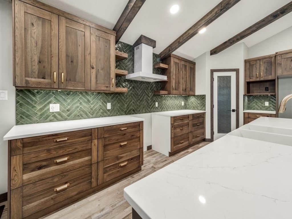 Kitchen with wooden cabinets, white countertops, and a green herringbone tile backsplash. Exposed beams and soft lighting create a cozy atmosphere.