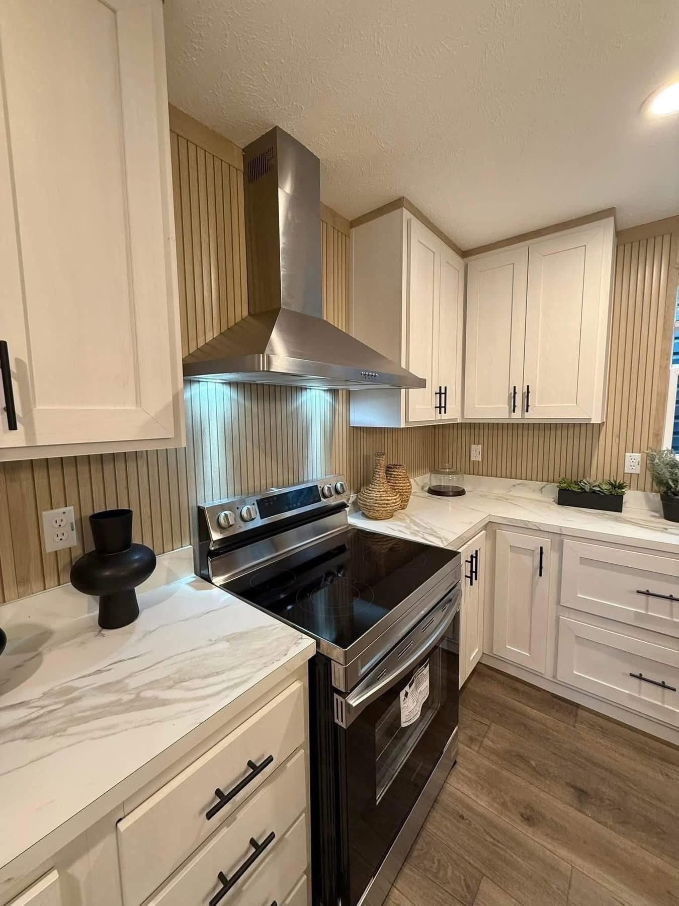 Modern kitchen with white cabinets, stainless steel stove, and range hood. Marble countertops and wooden accents create a warm, inviting space.