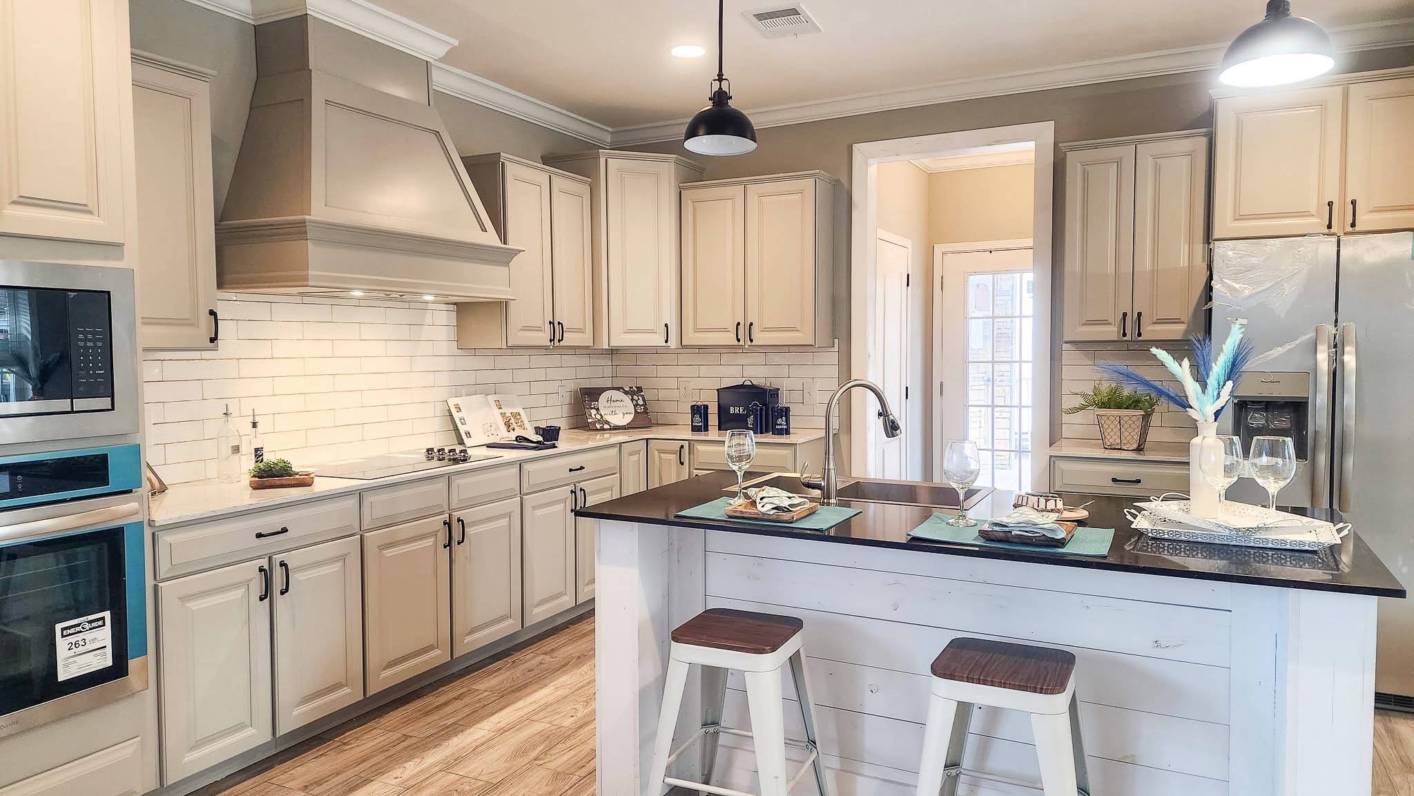A spacious kitchen with cream cabinets, stainless steel appliances, and a central island with two stools. The atmosphere is modern and inviting.