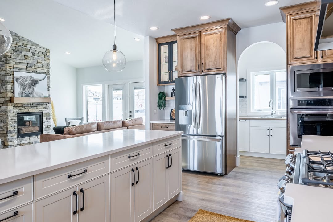 Bright modern kitchen with white cabinets, stainless steel appliances, and wooden accents. Spacious island, stone fireplace, and cozy living area.