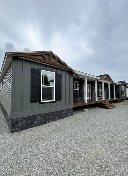 A modern, gray modular home with white trim and black shutters. The house has a covered porch and steps, set against an overcast sky, conveying a serene atmosphere.