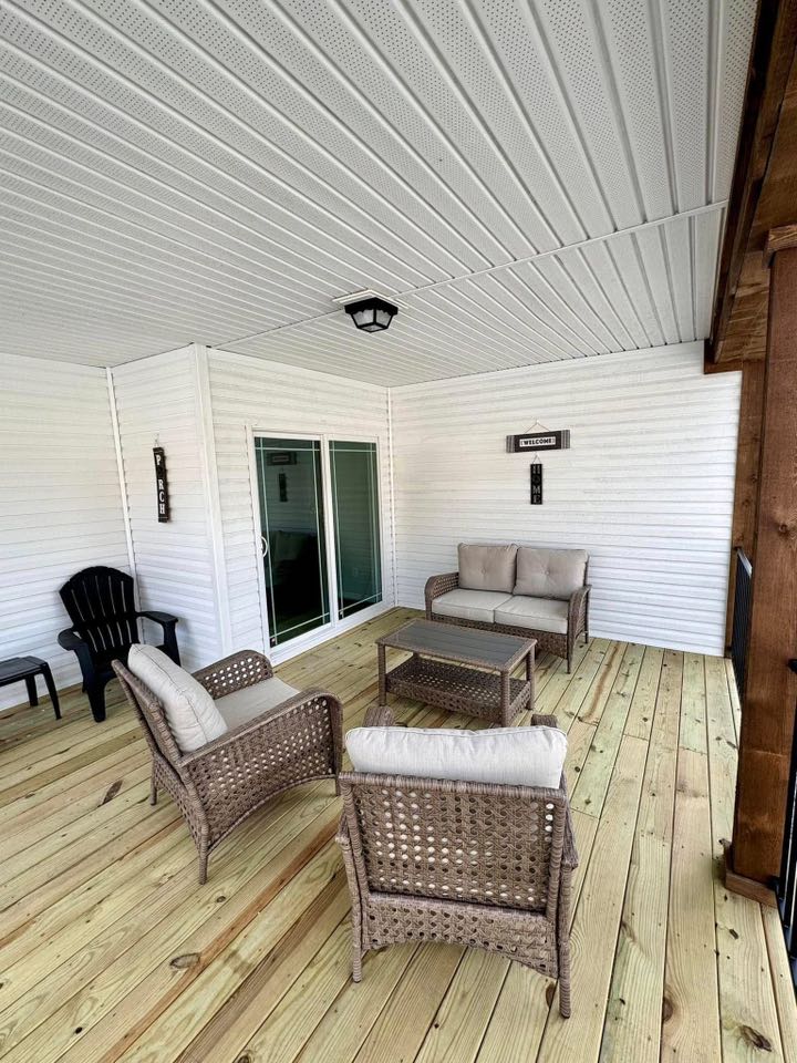 Cozy patio with wicker furniture on a wooden deck. A loveseat and chairs surround a small table. The white siding and "Welcome" sign add a warm touch.