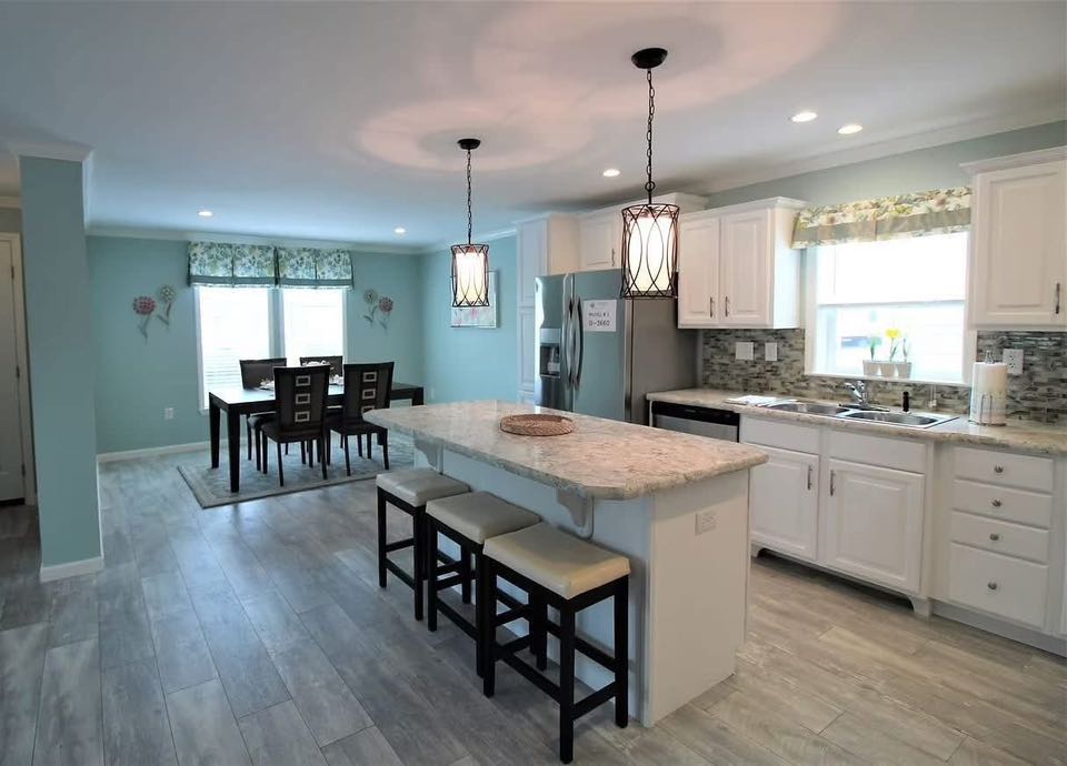 Spacious kitchen with white cabinets, marble island with three stools, and elegant pendant lights. Adjacent dining area with wooden table and chairs.