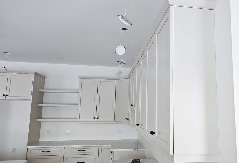 White kitchen with modern cabinets, open shelves, and a partial view of counters. Uninstalled ceiling lights dangle, suggesting ongoing renovations.