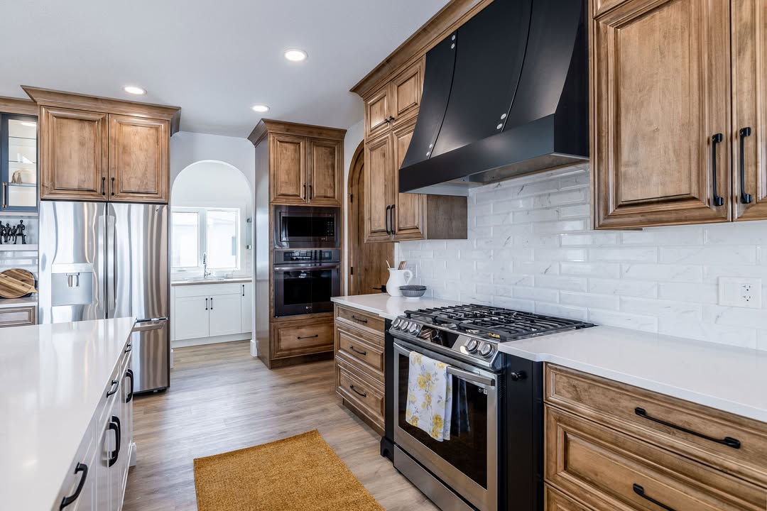 Warm, inviting kitchen with wooden cabinets, stainless steel appliances, and a black range hood. White subway tiles and ample natural light enhance elegance.