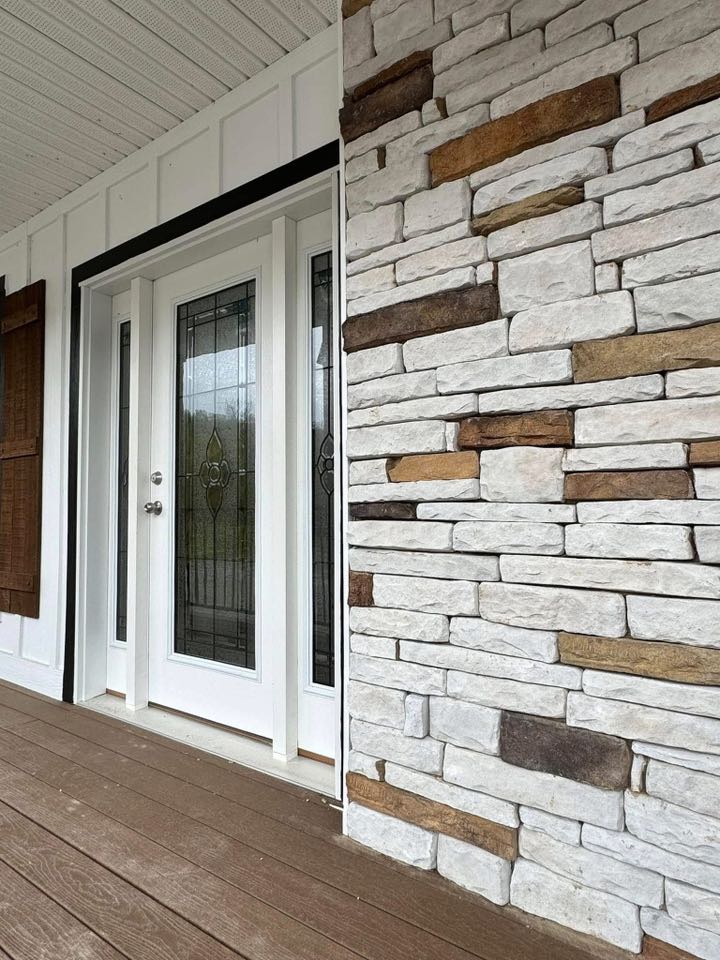 A white-framed glass door with decorative panes is next to an exterior wall made of textured stone in various shades of white and brown. The wooden porch floor adds warmth.