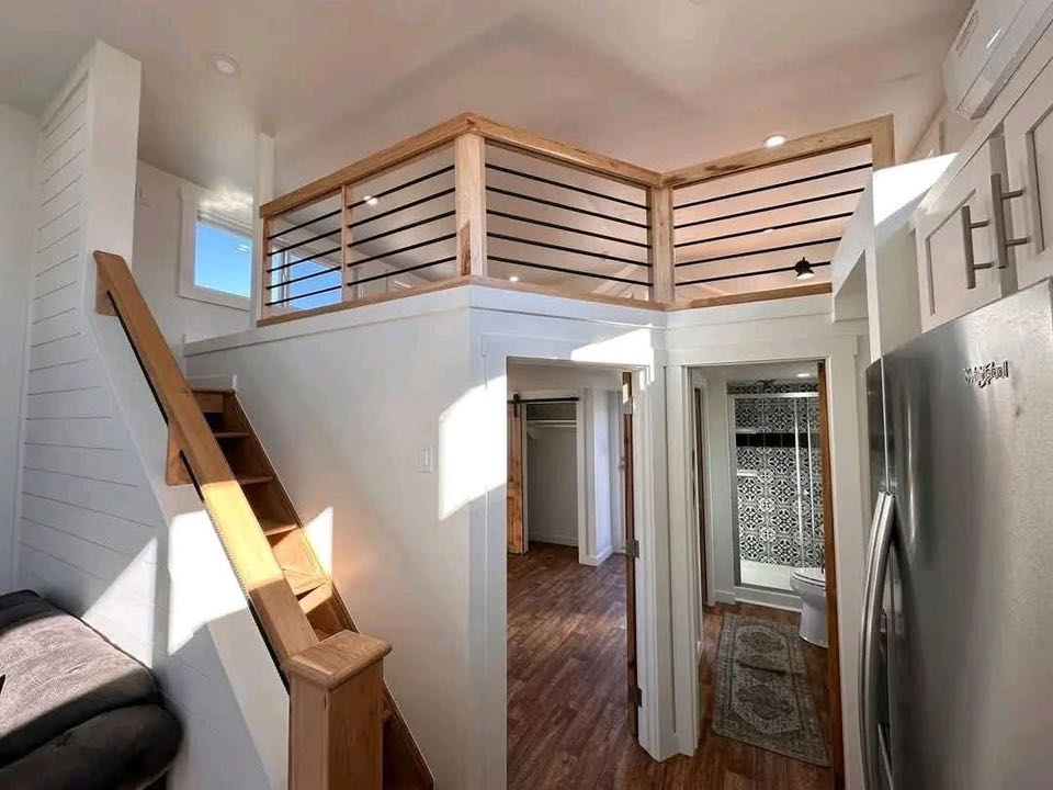 Small, modern loft space with wooden stairs leading to an upper level. Bright, natural light illuminates a sleek design and a cozy atmosphere.