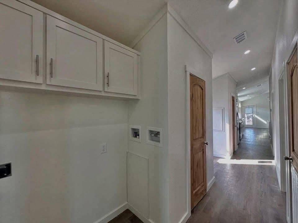 Hallway with white cabinets and wooden doors beside a utility area. Sunlight streams in, highlighting the dark wood floors, creating a warm ambiance.
