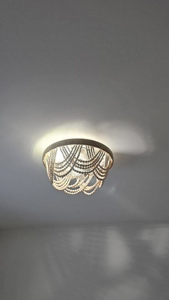 A ceiling light fixture with cascading strands of beads creating a vintage, elegant look. Soft lighting casts gentle shadows on a plain white ceiling.