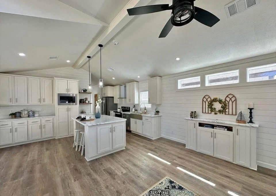 Spacious kitchen with white cabinets, island with hanging lights, and hardwood floors. Bright with windows, modern appliances, and a cozy farmhouse decor.