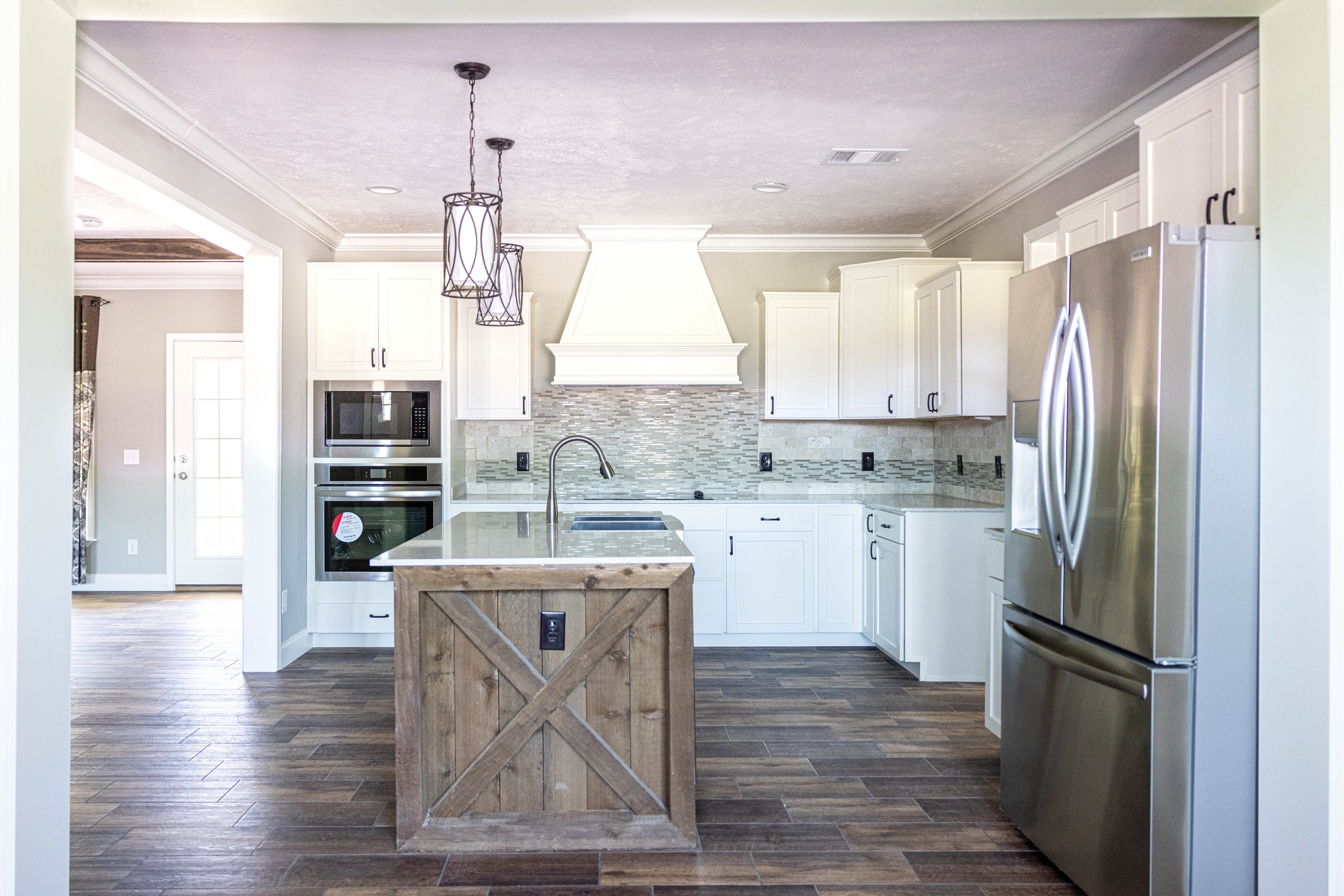 Modern kitchen with white cabinets, a stainless steel fridge, and a wooden island. Pendant lights hang above, and dark wood flooring adds warmth.