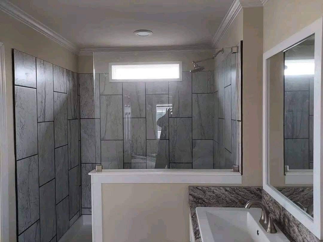 Modern bathroom with a large, tiled shower featuring gray slate tiles. There is a rectangular window above and a white countertop with a silver faucet.