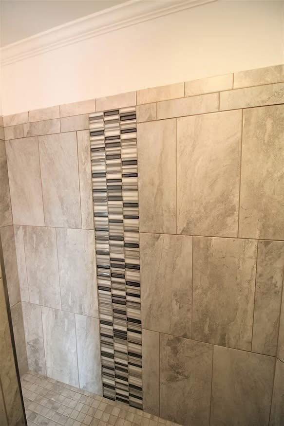 Modern shower wall with large beige tiles and a vertical strip of small, multicolored tiles in black, gray, and white, creating a sleek, stylish look.