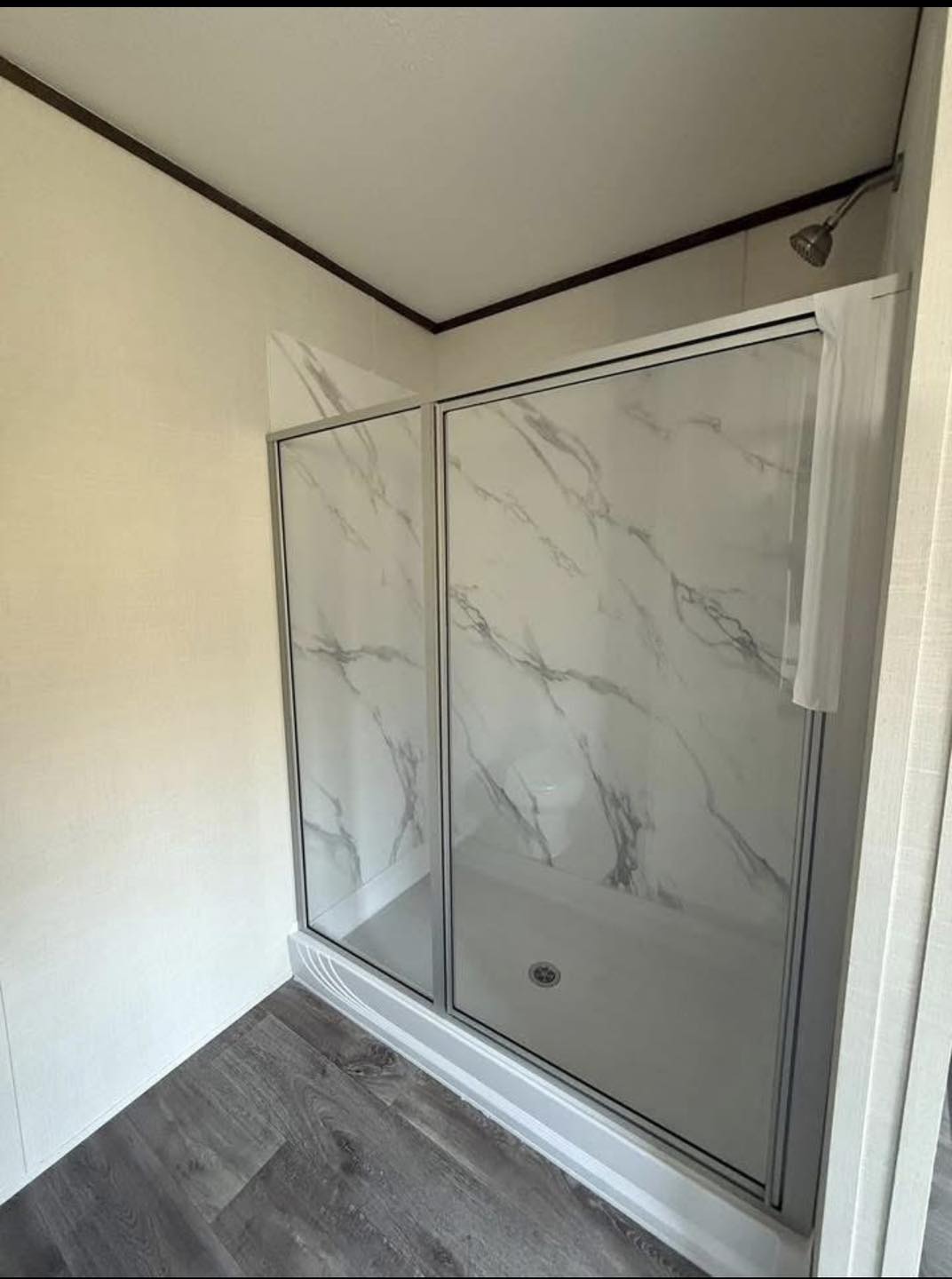 Modern shower with glass doors and marble-patterned walls, set in a bathroom with light walls and dark wood flooring, creating a clean, sleek feel.