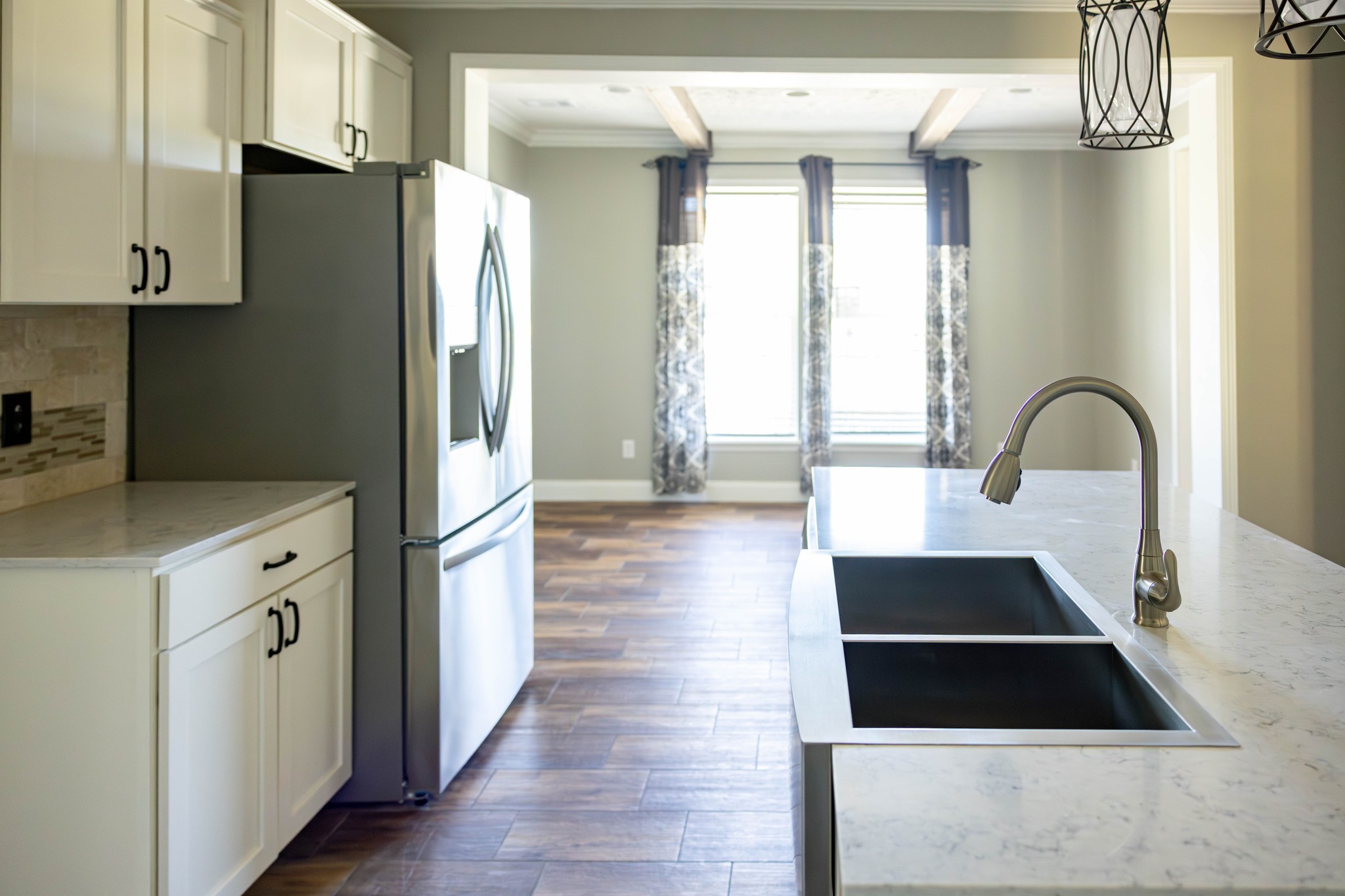 Modern kitchen with white cabinets, a mosaic tile backsplash, and stainless steel appliances. Features a central island and wood-patterned tile floor.