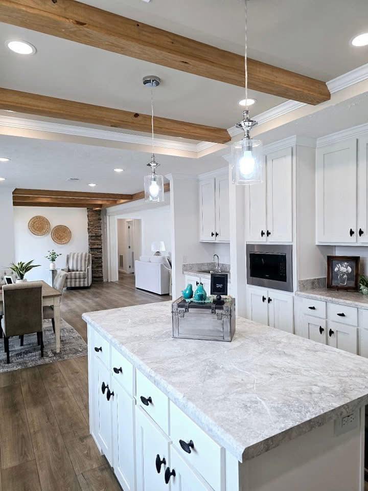 Spacious kitchen with white cabinets and a marble island, pendant lights, and wooden beams. Adjacent dining area with modern decor, warm and inviting.
