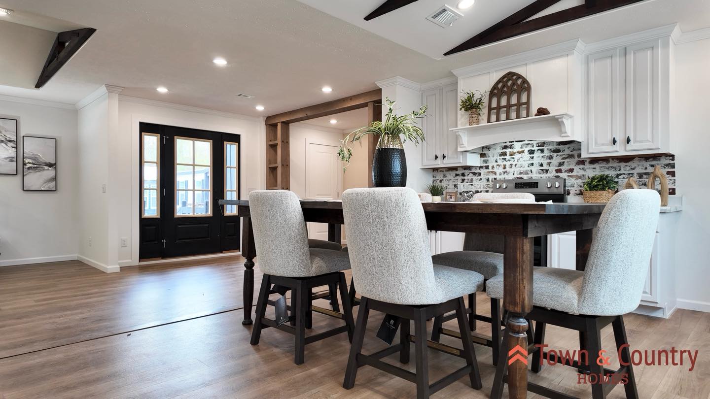 Spacious, modern kitchen with white cabinets, brick backsplash, and wooden beams. A dark wood dining table with four upholstered chairs adds elegance.