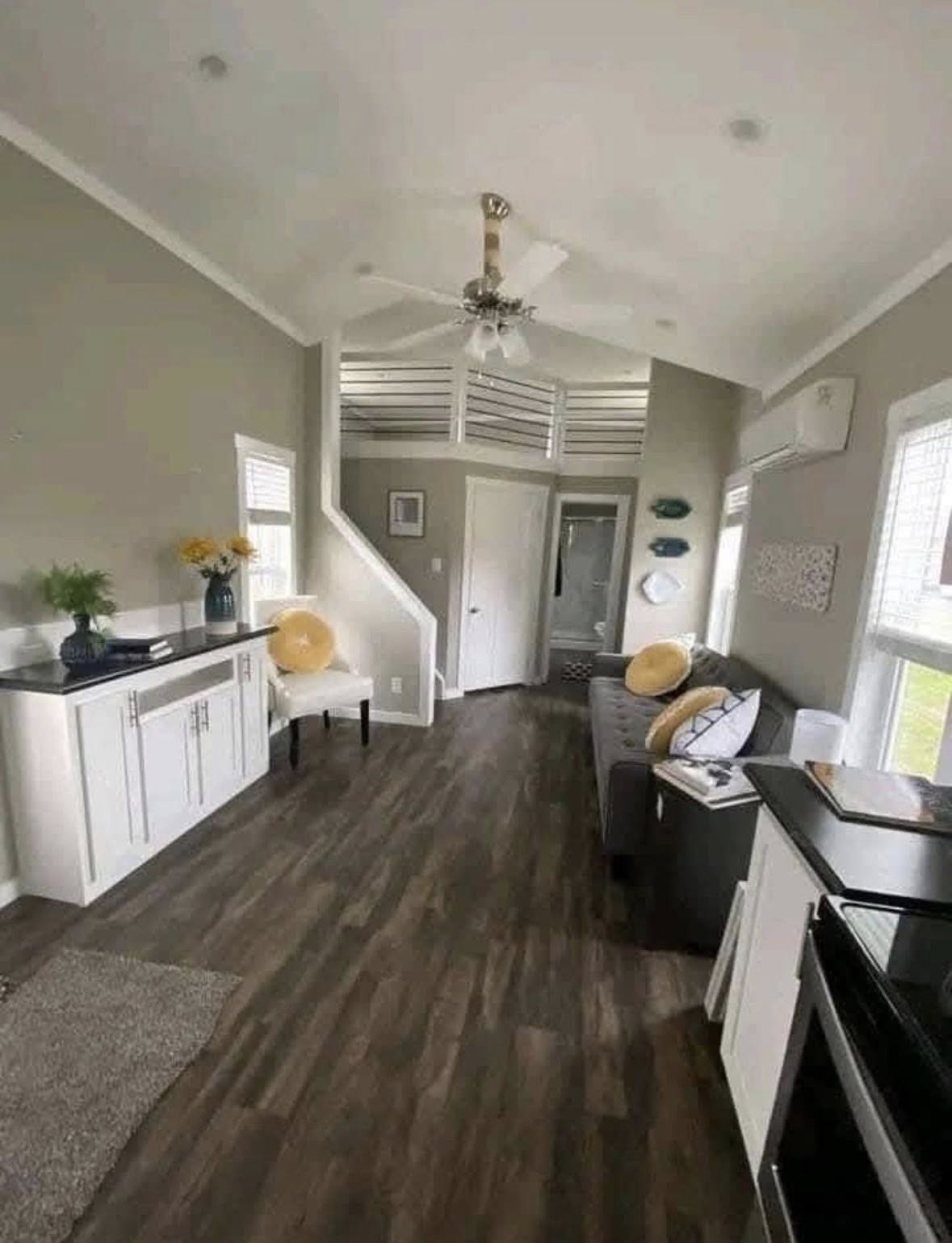 A cozy gray and white living room, featuring wood flooring, a ceiling fan, and modern decor. Yellow accents add brightness and warmth to the space.