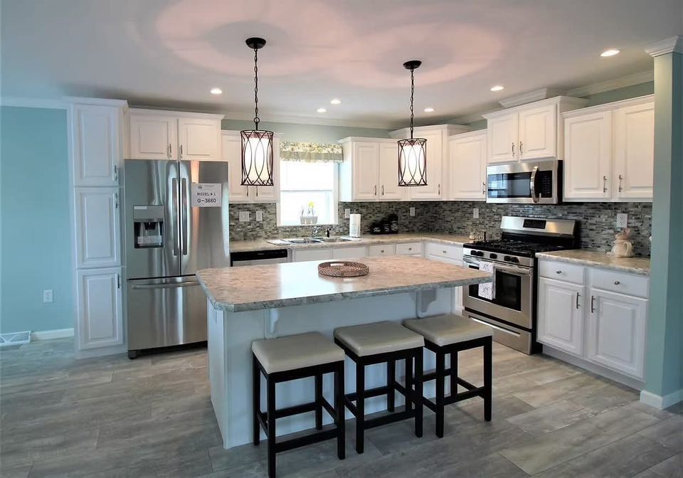Modern kitchen with white cabinets, stainless steel appliances, and tiled backsplash. Features a large island with stools and elegant pendant lighting.