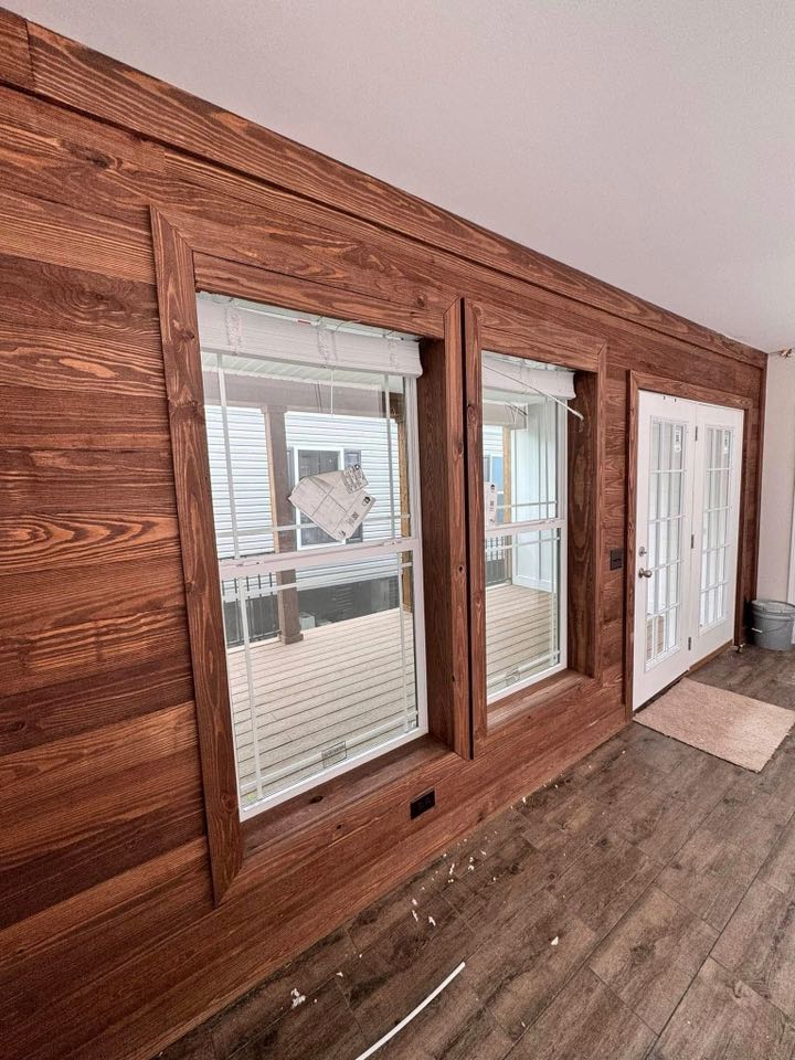 Wood-paneled wall with two vertical windows and a glass door. Natural light enters, highlighting the warmth of the wood. Relaxed, cozy atmosphere.
