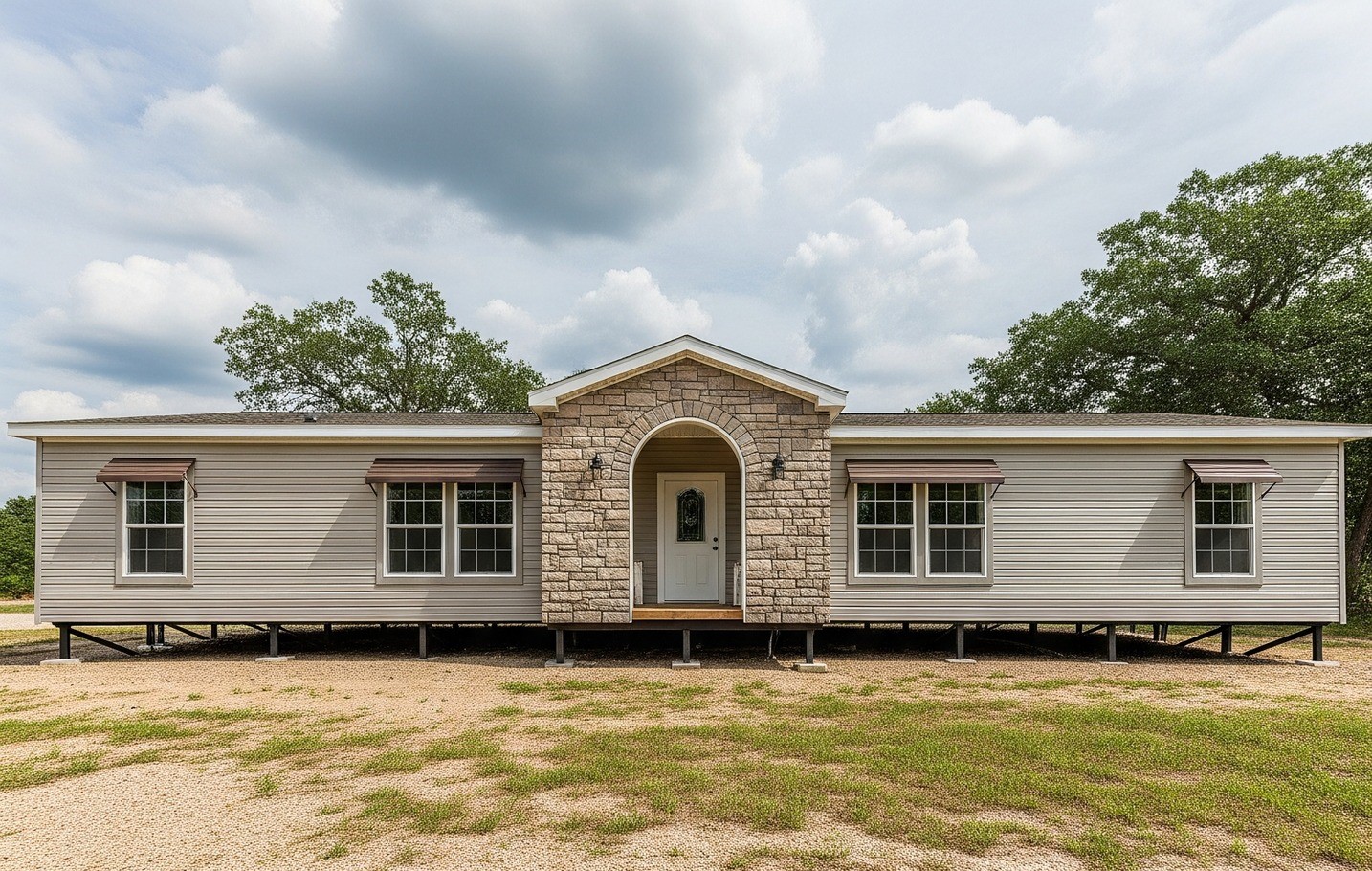 A modern modular home with stone entry, beige siding, and symmetrical windows sits on a grassy lot under a partly cloudy sky, conveying a serene, inviting feel.