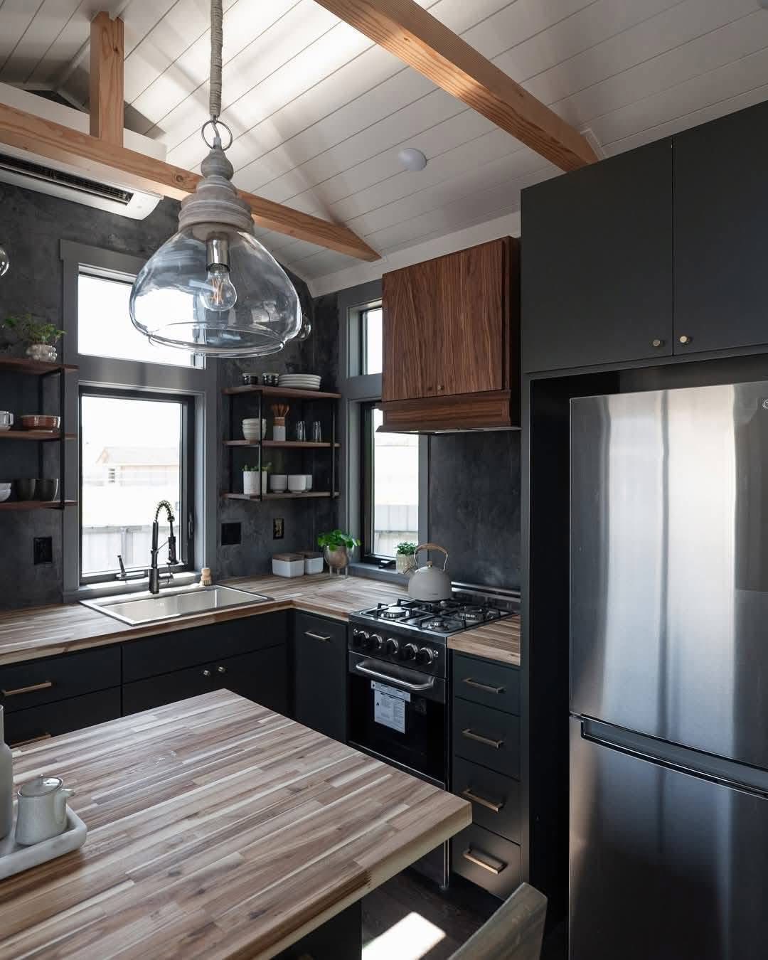 Modern kitchen with wooden countertops, black cabinetry, and stainless steel appliances. Large glass pendant light hangs from the ceiling, creating a cozy and stylish atmosphere.