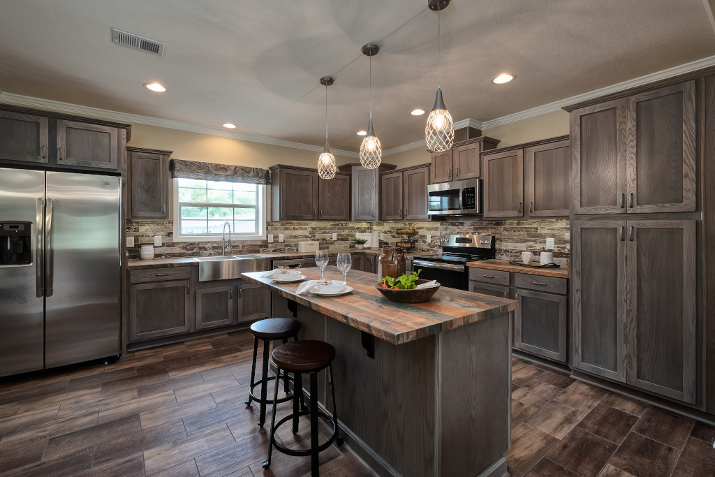 Spacious kitchen with rustic wood cabinets, stone backsplash, and a central island. Three pendant lights hang above, creating a warm, inviting atmosphere.