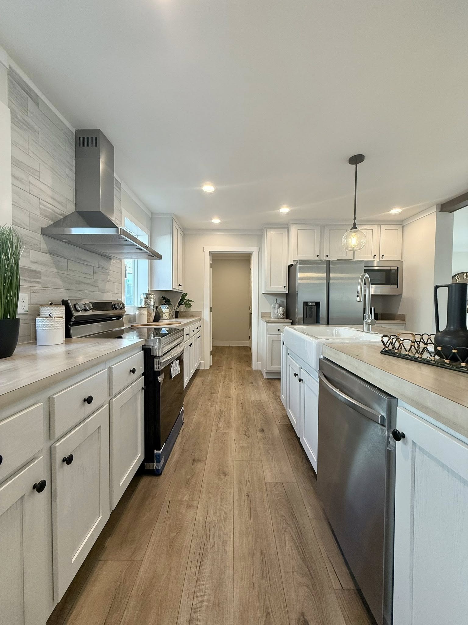 Bright modern kitchen with wood flooring, white cabinets, stainless steel appliances, and pendant lighting. A welcoming and sleek atmosphere.